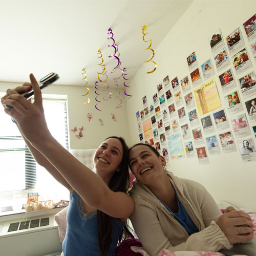 A group of Molloy University students, smiling and taking a selfie together in a residence hall.