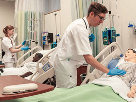 Two medical students practicing patient care in a hospital room simulation. 