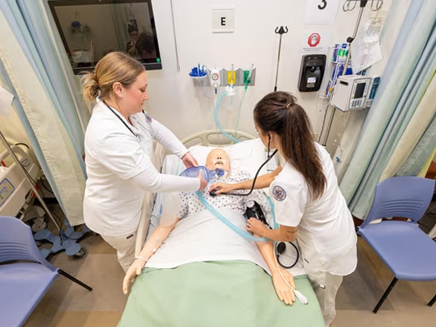 Nurses Emily Thompson and Catherine Zaharis, recent graduates of Molloy University's nursing bachelor of science degree program, practice in Molloy's new simulation lab, which has high-tech mannequins that nurses use in training