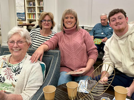 Geraldine Burchell Dwyer Riveiro, her daughters and grandson sit together smiling in a cozy living room. 