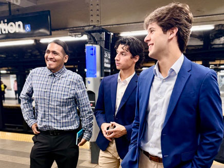 3 business students stand on a subway platform, smiling