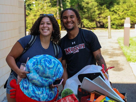 Students/Family with a cart full of belongings. The woman on the left is holding a large plush crab and the man on the right is wearing a Molloy Lions shirt.