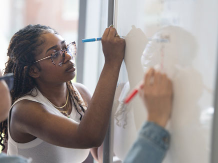 Two women are writing on a whiteboard.