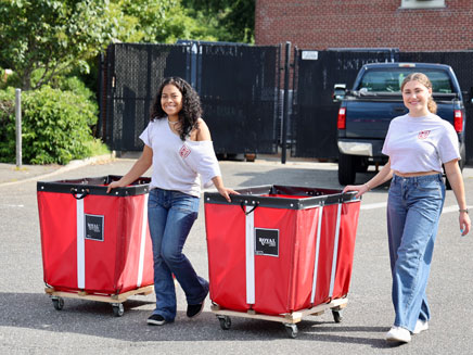 Two female students pushing red move in day carts wearing Molloy University t-shirts