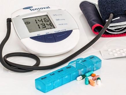 Digital blood pressure monitor with reading, a weekly pill organizer filled with pills.