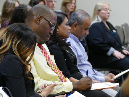 A group of adults seated in a conference, attentively listening and taking notes