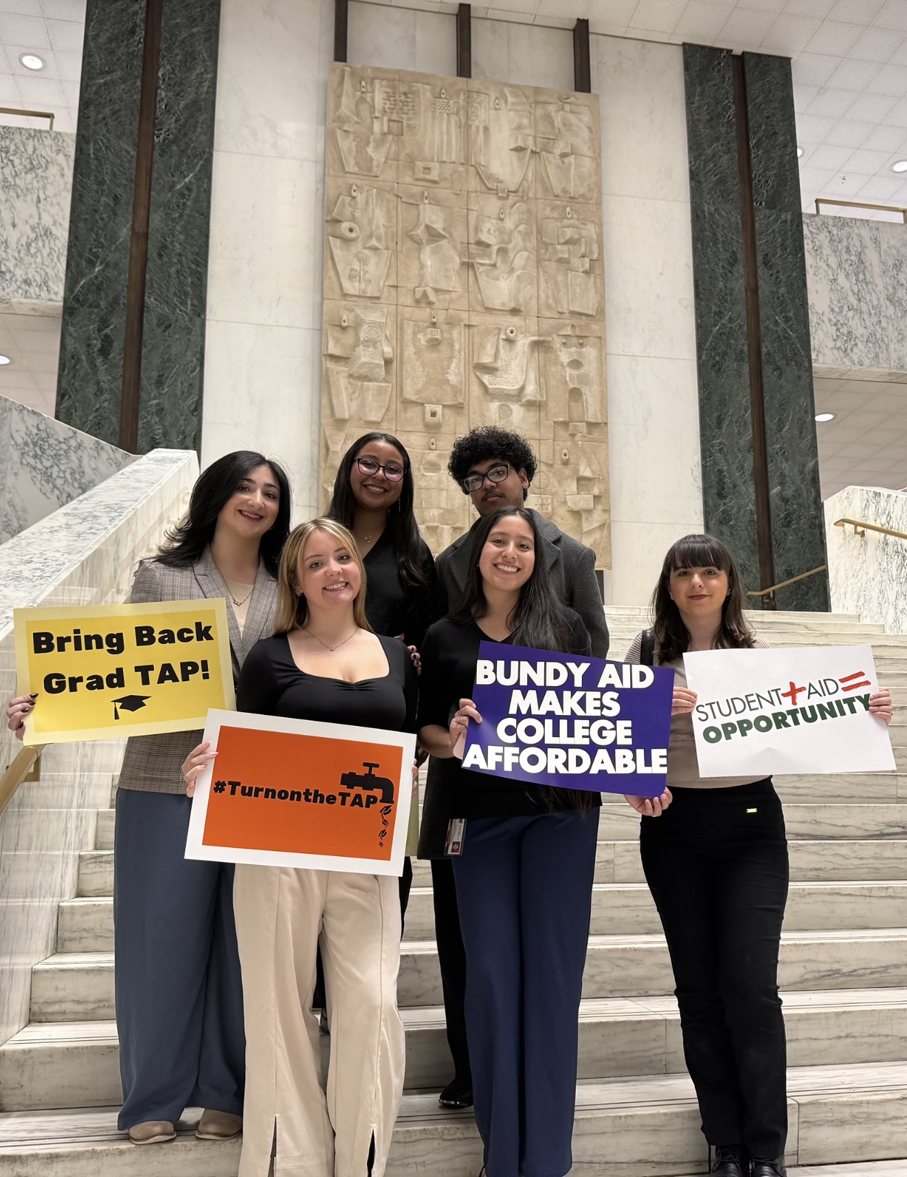 Molloy students holding signs that read: "Bring Back Grad TAP", "#Turn on the TAP", "Bndy Aid makes college affordable", and "Student + Aid = Opportunity"