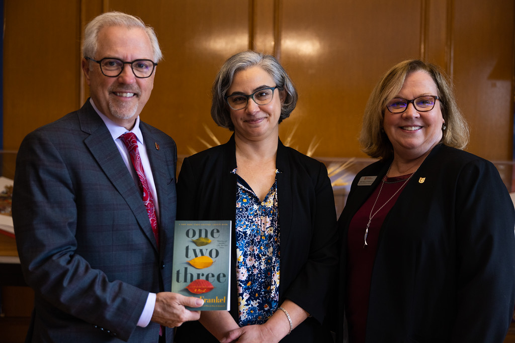 A picture of President James Lenti holding a book standing next to author Laurie Frankel and provost Michelle Piskulich at Molloy University