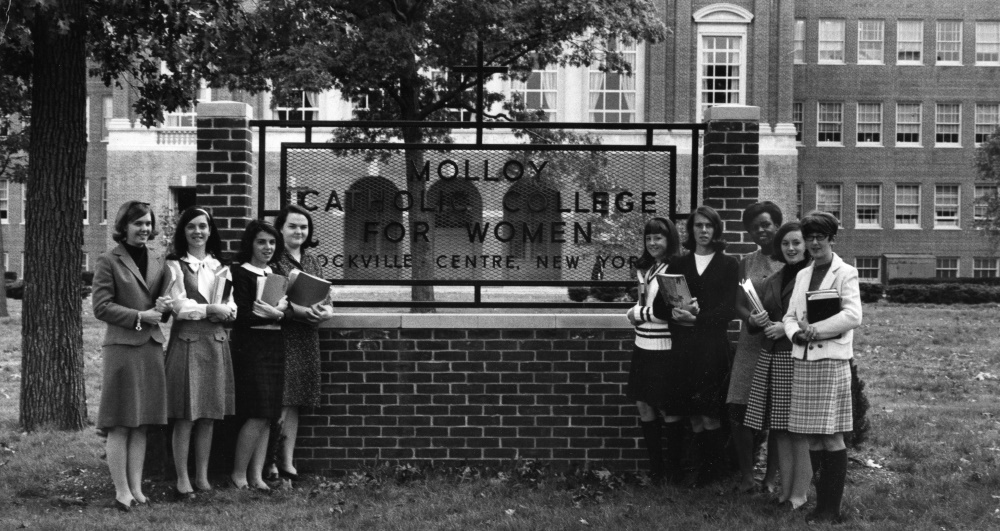 black and white photograph of nine women outside the molloy college sign
