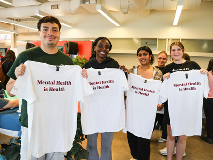 4 students holding up T-shirts reading "Mental Health is Health" 